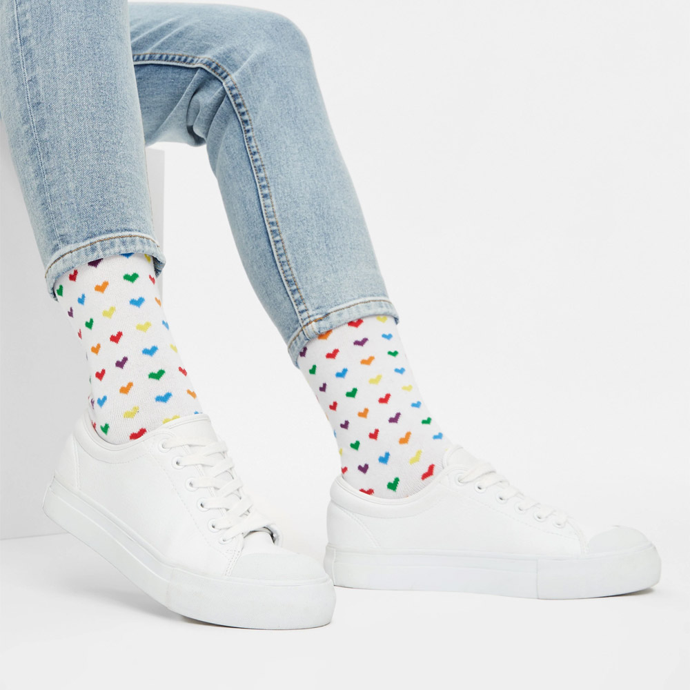 Person trägt weißes Sneaker und weiße Socken mit bunten Rainbow Herzen